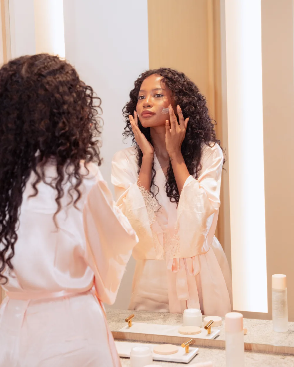 Model applying LUMI cream at a warm-lit vanity
